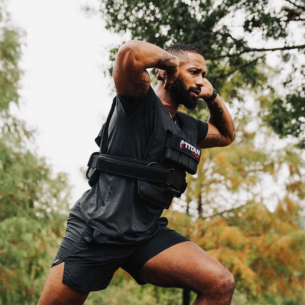 Person exercising outdoors wearing a black Titan Fitness weighted vest with broad straps around the torso