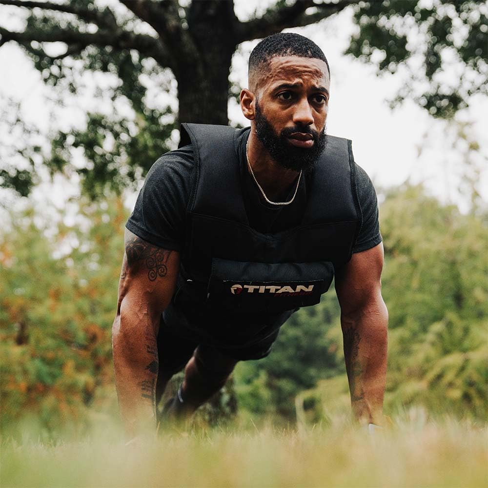 Person wearing a black Titan weight vest in a push-up position on grass