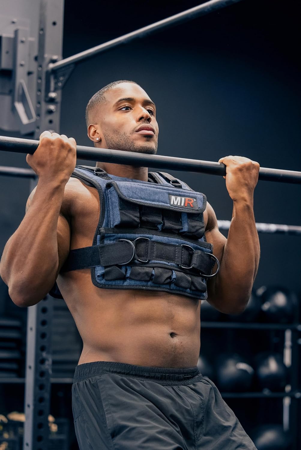Person wearing a miR weighted vest while gripping a gym bar with front pockets and waist straps visible